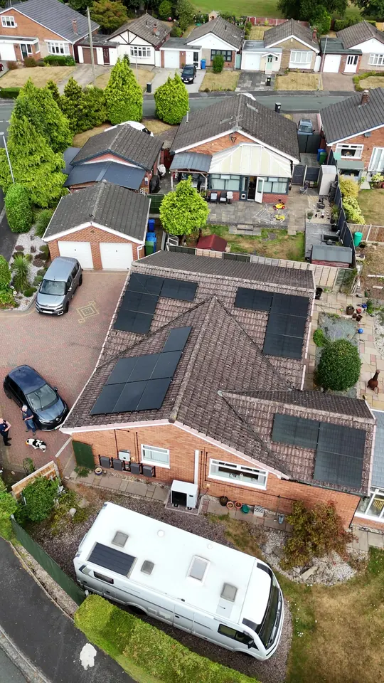 Oblique drone view of a bungalow with solar panels on three visible roof faces and an air source heat pump on the side wall