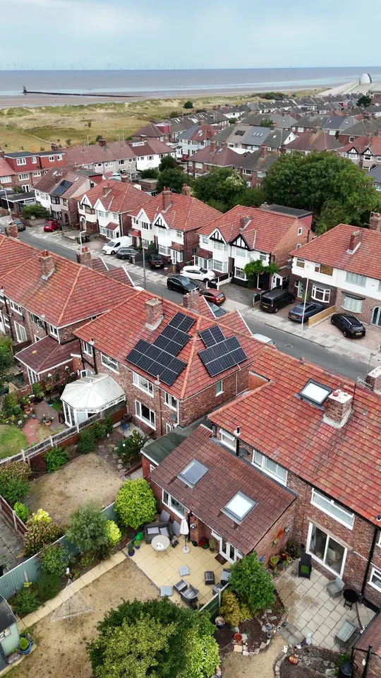 Drone view of solar panels on a red-tiled semi-detached house with the Irish Sea and an offshore wind farm behind