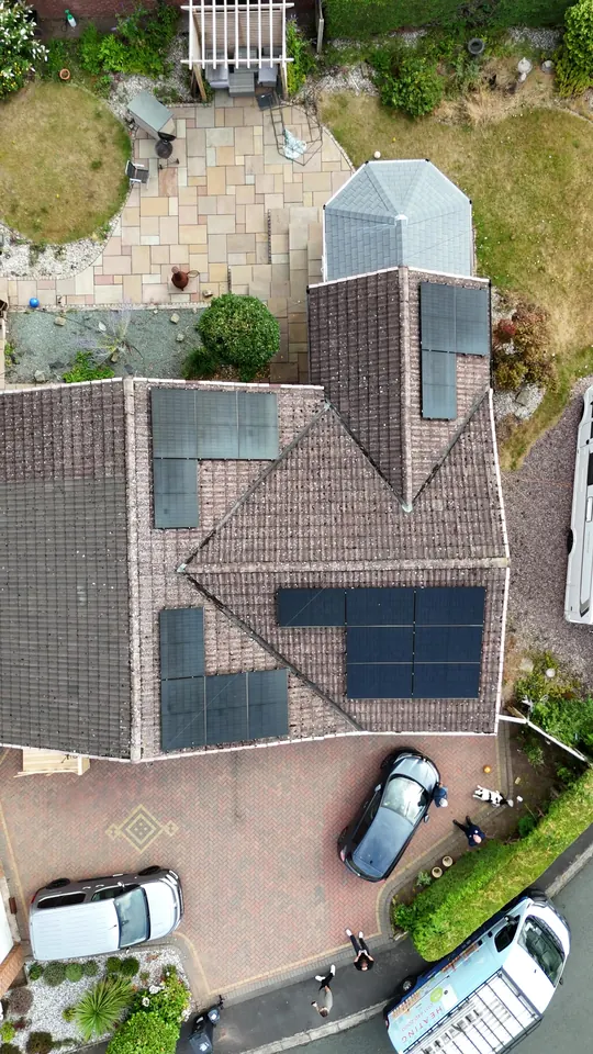 Top-down drone view of the same bungalow showing panel arrays on four roof faces around the conservatory